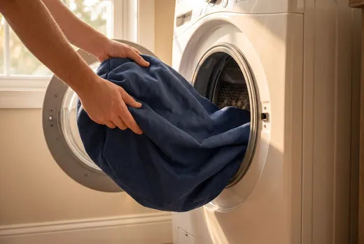 Hands loading the navy machine-washable Everyday Bed cover into a front-loading washing machine